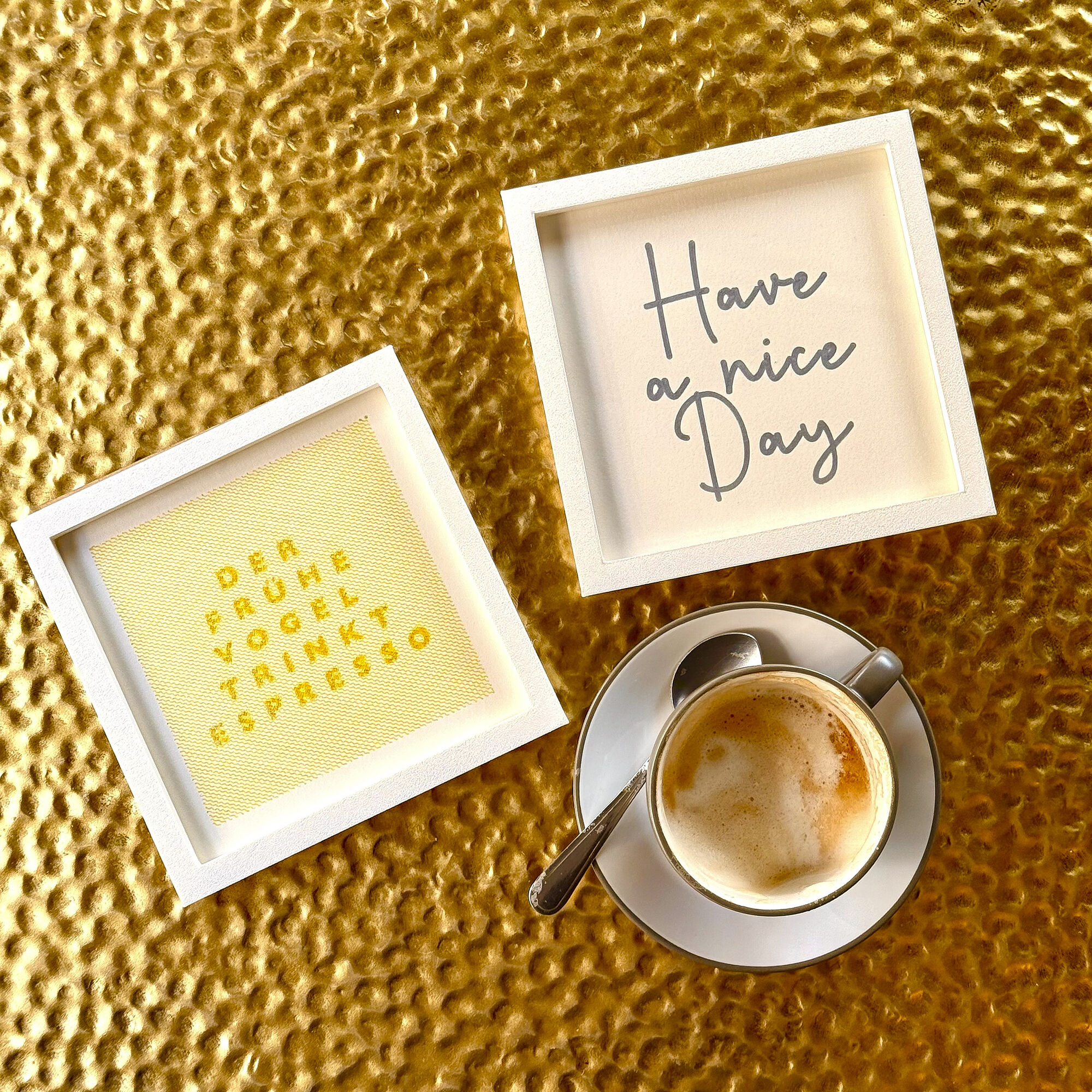 Zwei gerahmte Typo-Editionen auf goldenem Untergrund neben einer Tasse Espresso — Beispiel für ein mehrteiliges Kundengeschenk-Set
