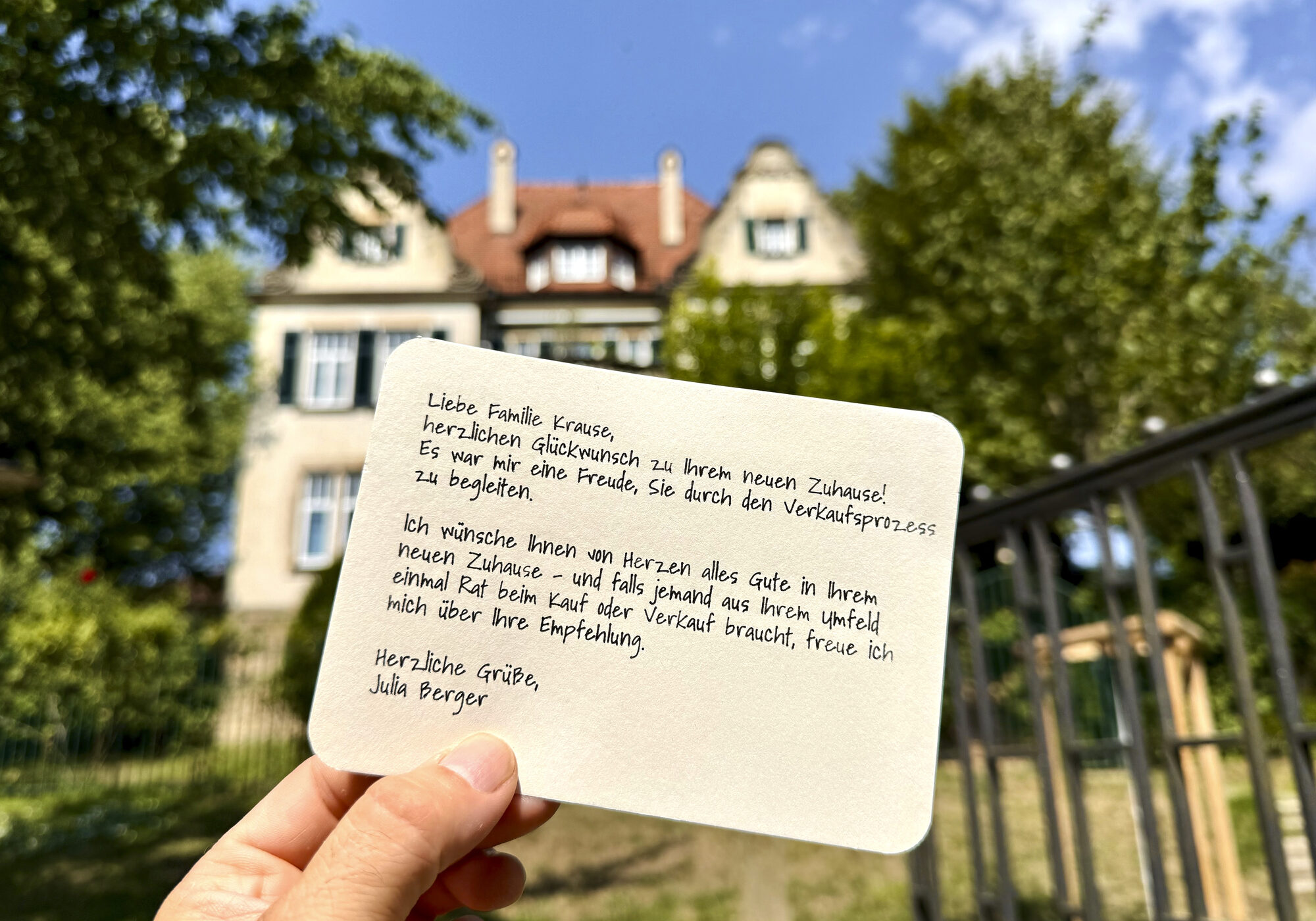 Handgeschriebene Dankeskarte eines Immobilienmaklers an eine Familie nach Hauskauf, gehalten vor dem verkauften Haus