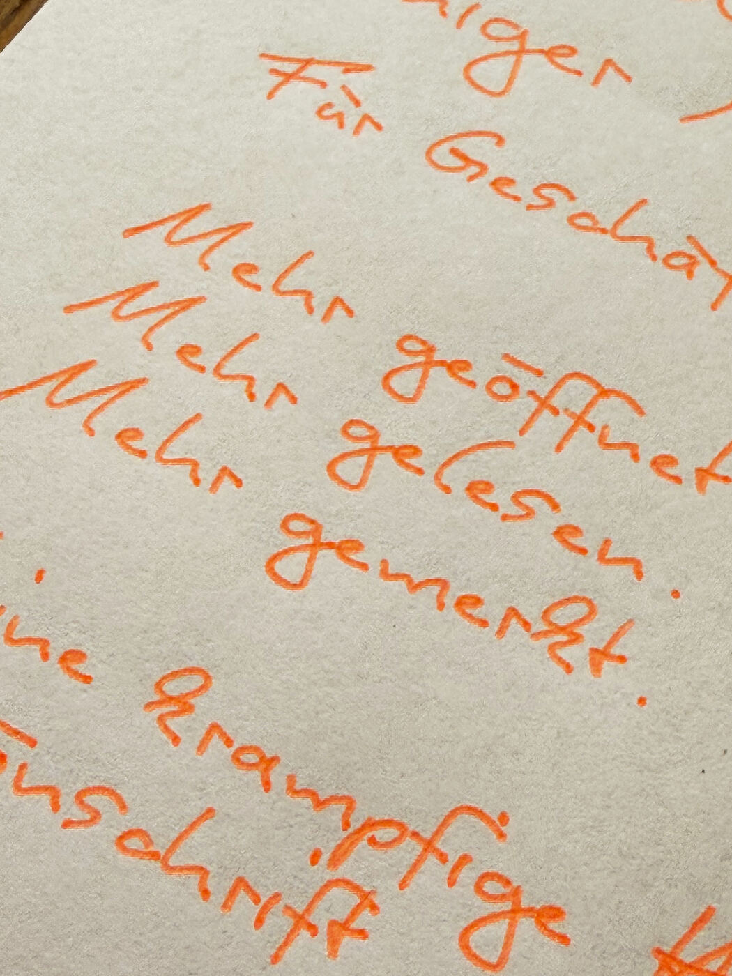 Nahaufnahme handgeschriebener Text mit orangem Stift: Mehr geöffnet, mehr gelesen, mehr gemerkt