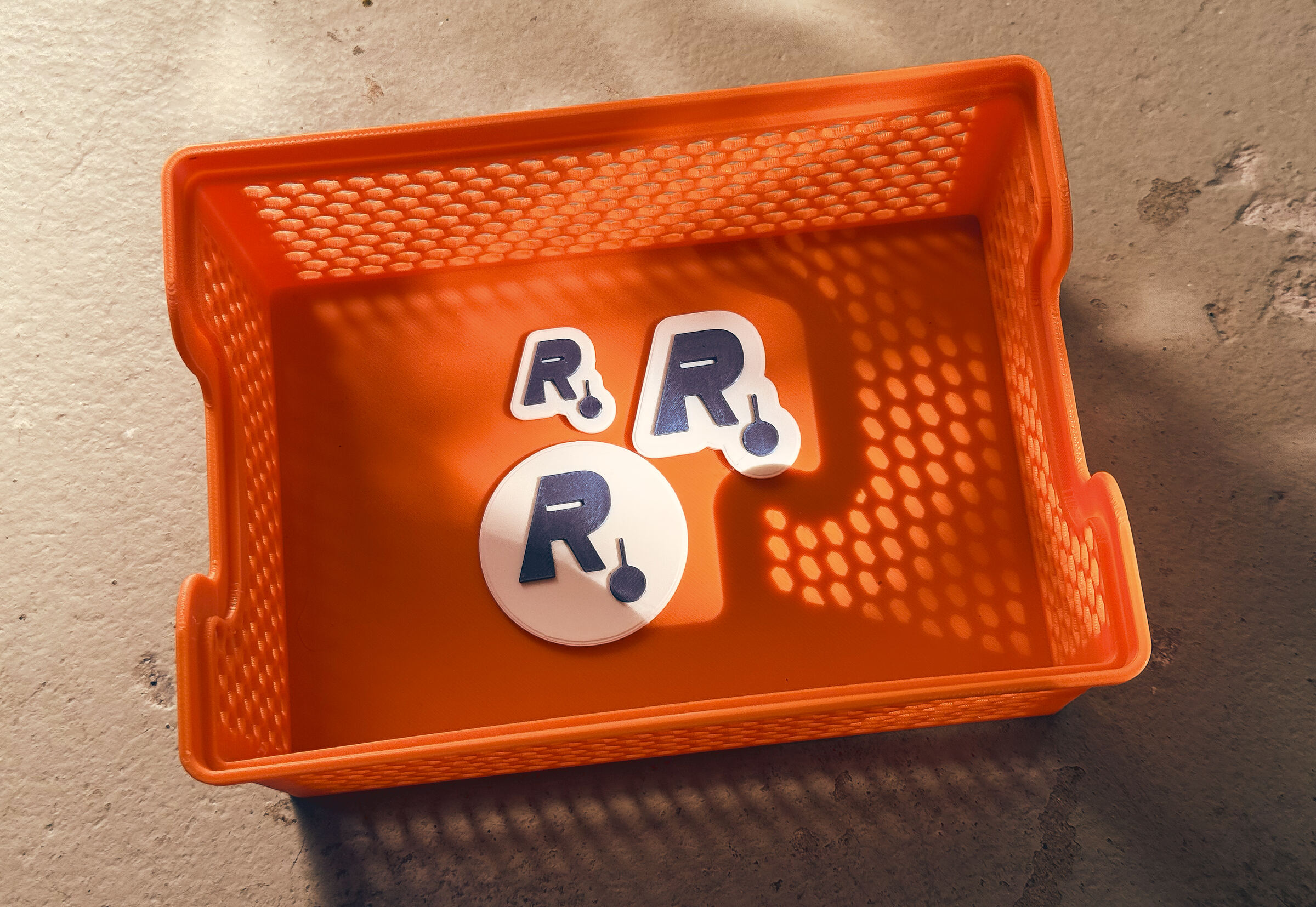 Robo-Writer Logo als 3D-gedrucktes Objekt in drei Größen, im Streiflicht in einer orangen Werkstatt-Ablage