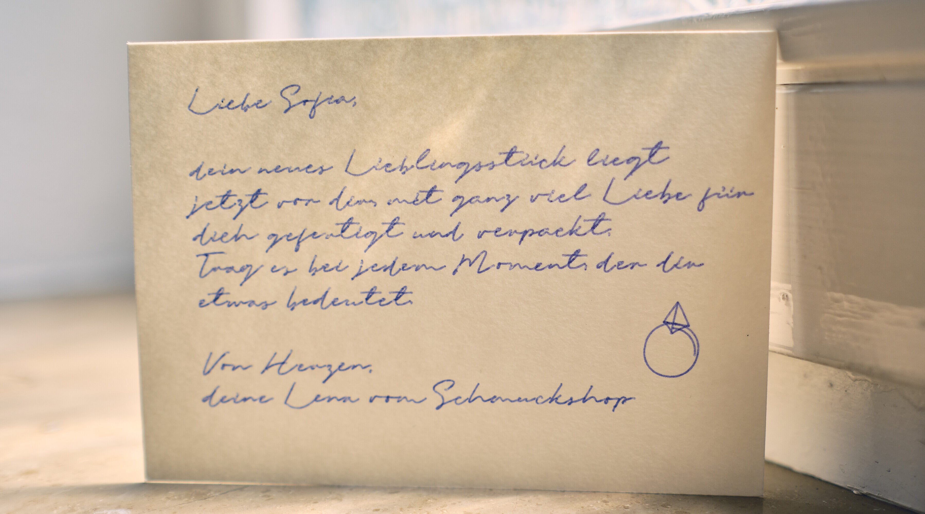 Handgeschriebene Dankeskarte für einen Schmuck-Onlineshop auf Fensterbank mit gezeichnetem Ring-Motiv